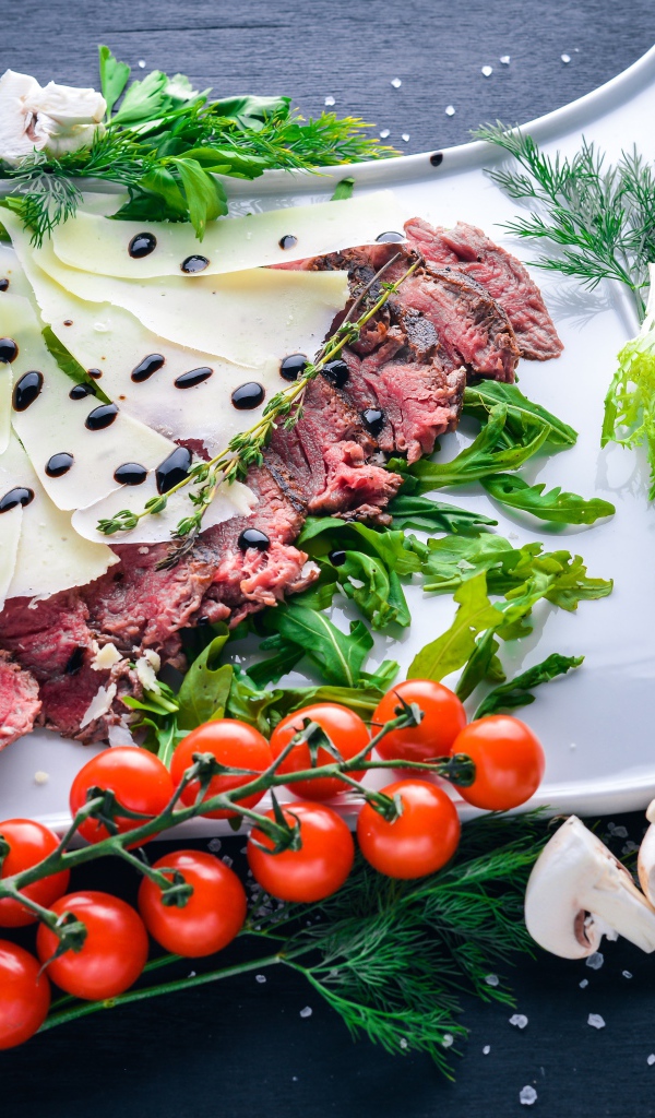 Мясо с сыром, овощами и зеленью на тарелке