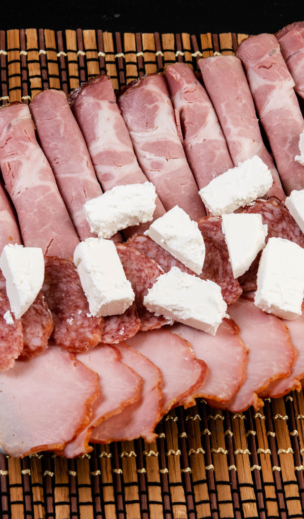 Колбаса и ветчина на тарелке с кусочками сыра фета