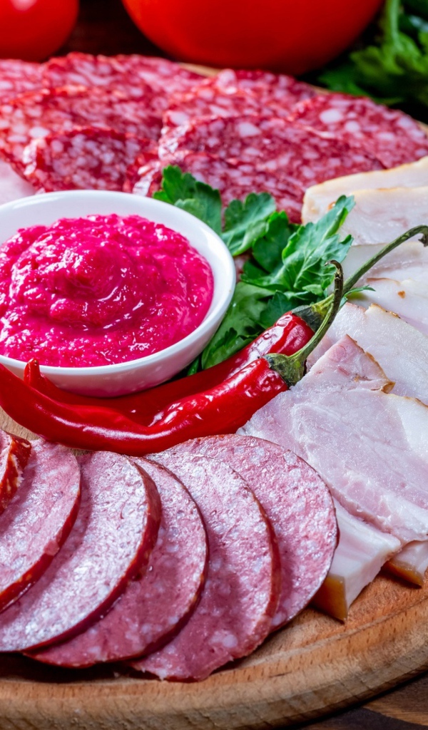 Мясная нарезка на доске с соусом, красным перцем,  помидорами и зеленью 