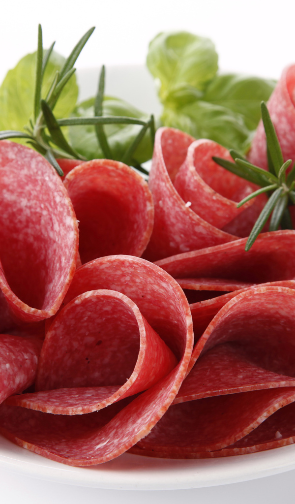 Тонкие кусочки колбасы на тарелке с зеленью 