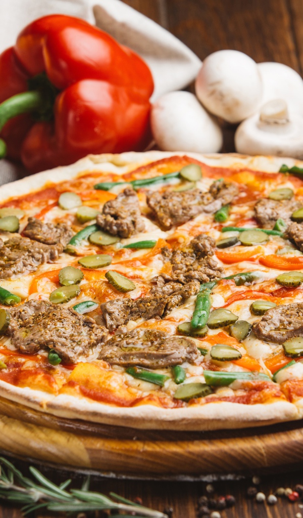 Свежая пицца с мясом и огурцами на столе с овощами