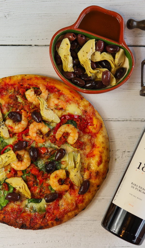 Пицца на столе с оливками и бутылкой вина
