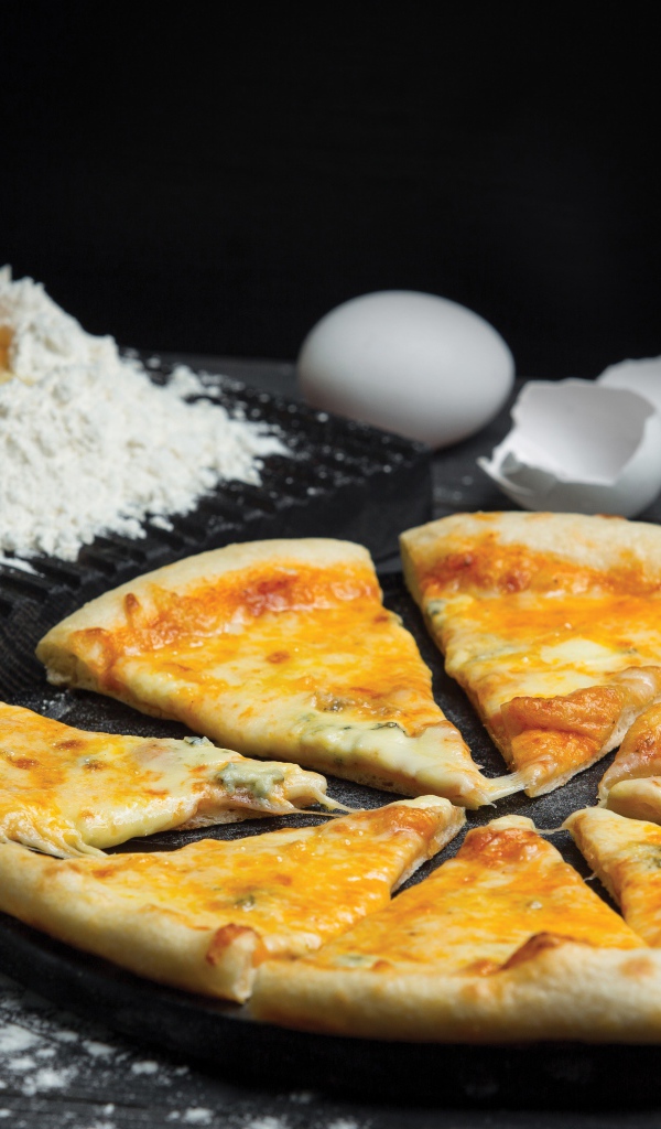 Пицца с сыром нарезана кусочками на столе с мукой и яйцами