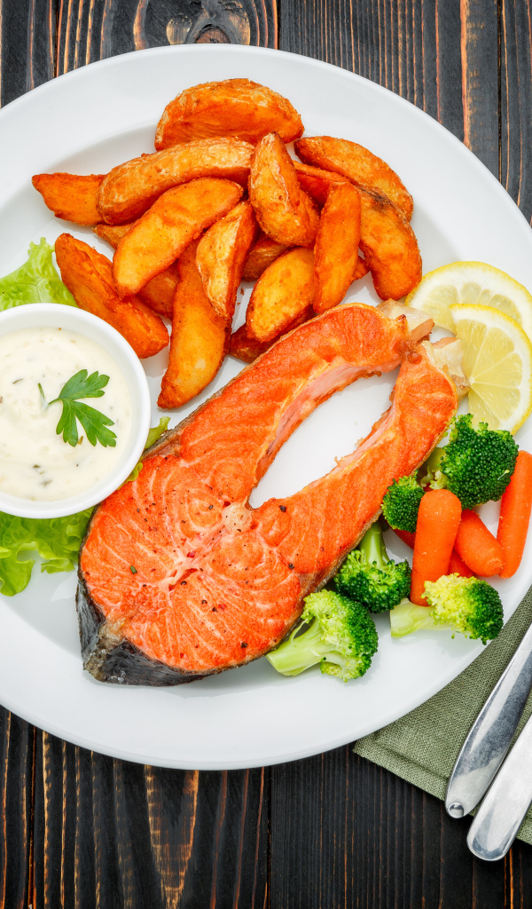 Кусок красной рыбы на тарелке с картофелем и соусом