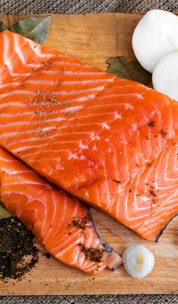 Куски красной рыбы на разделочной доске с луком и специями