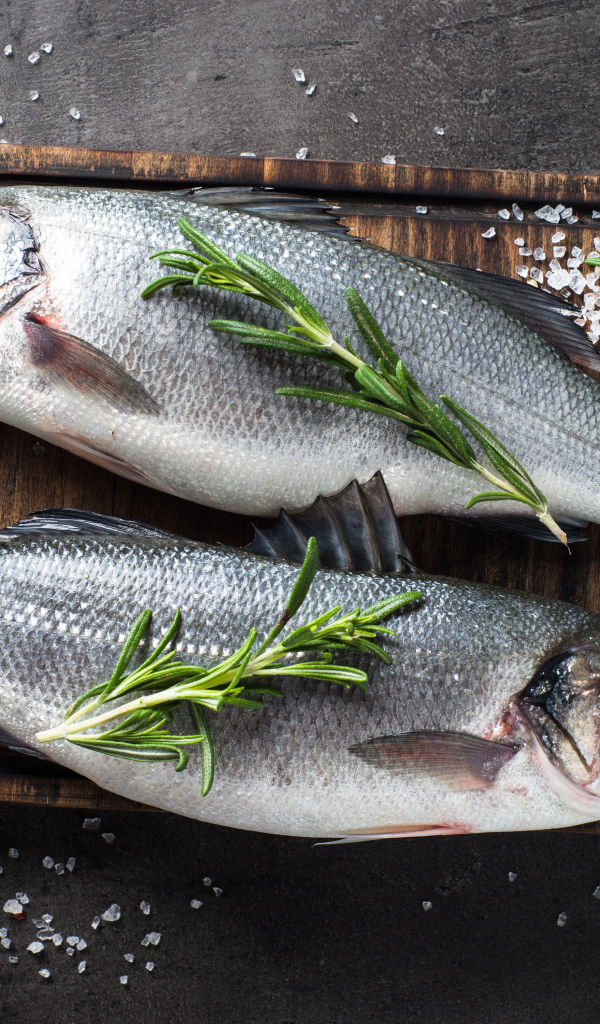 Две свежие рыбины на разделочной доске с солью и веточками розмарина