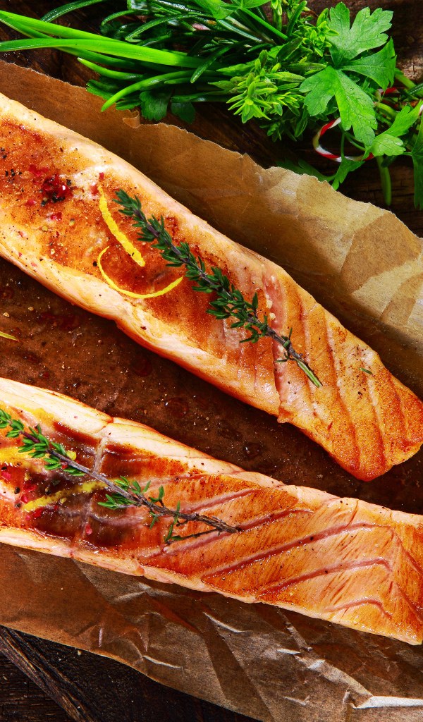 Два куска запеченной рыбы на столе с оливковым маслом и зеленью