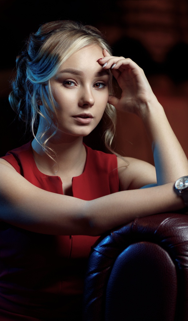 Красивая девушка с часами на руке сидит в кресле