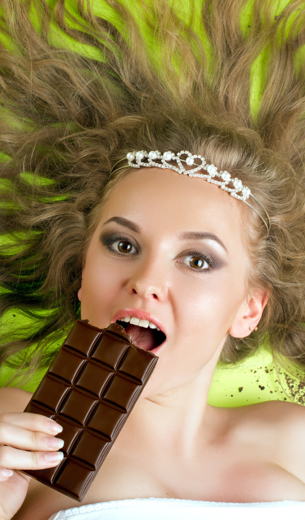 Красивая девушка с украшением в волосах лежит с шоколадкой 