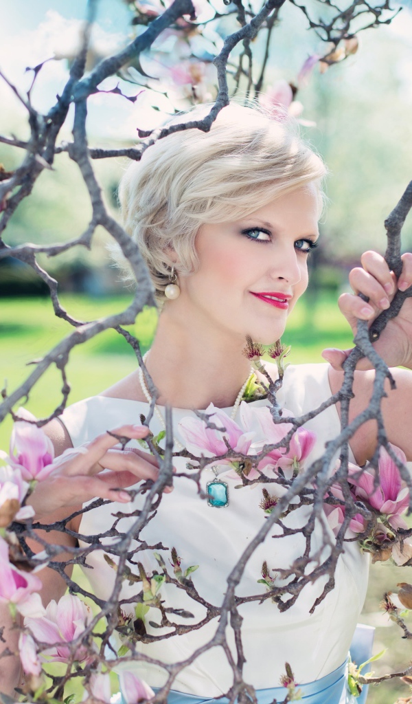 Красивая женщина с короткой стрижкой стоит у цветущей магнолии 