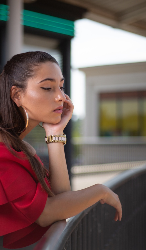 Задуманная девушка в красном платье стоит у перил 