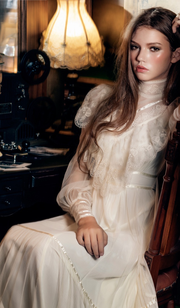 Девушка в красивом белом платье сидит на стуле у стола