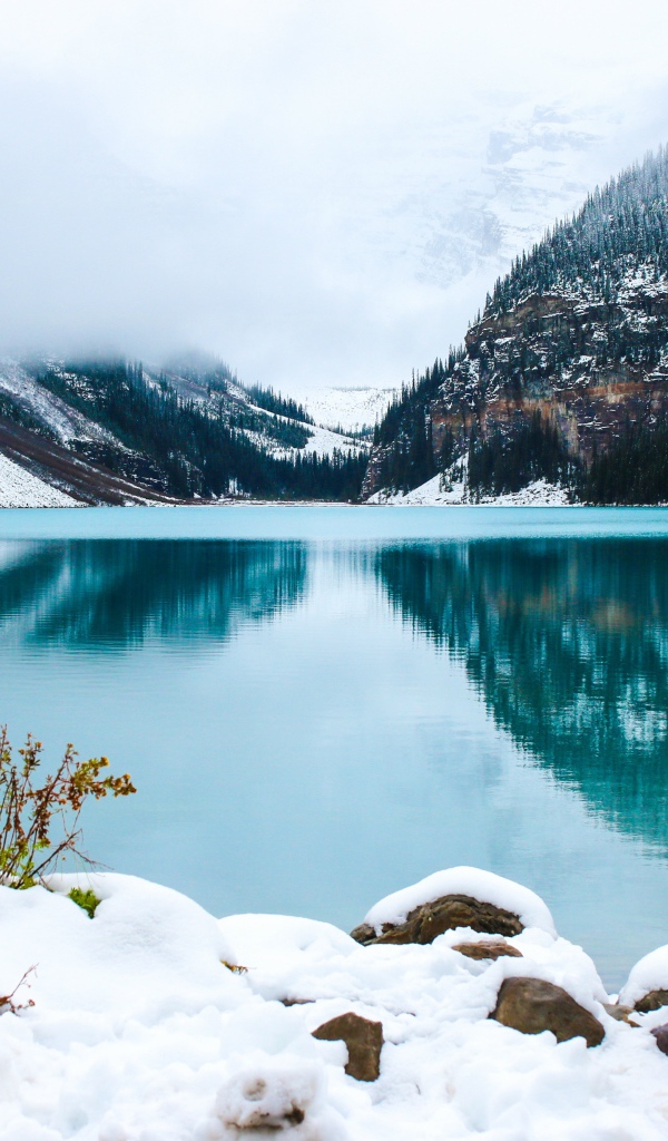Девушка стоит у голубого озера на заснеженном берегу 