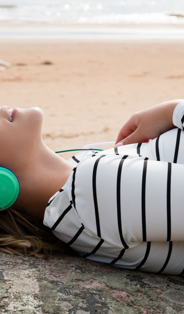 Молодая девушка лежит в наушниках на земле у моря