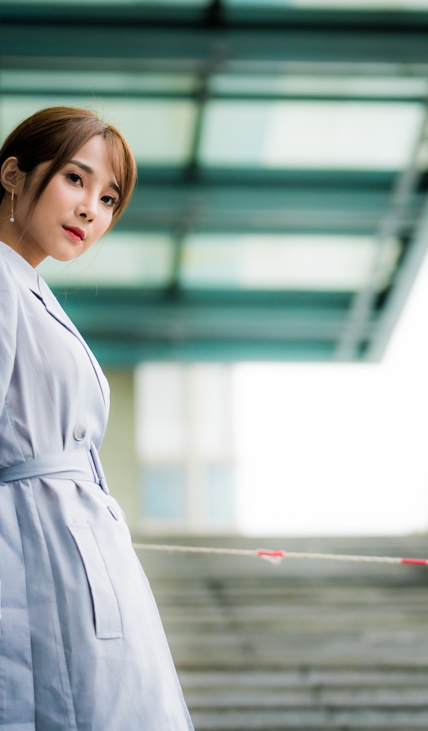 Девушка азиатка в пальто стоит у перил 