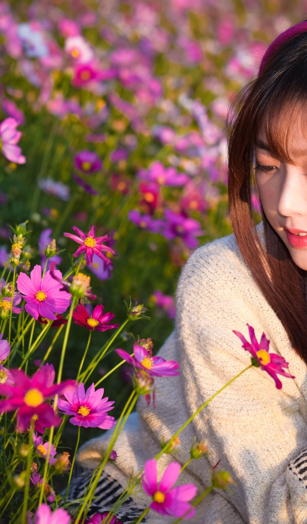 Девушка азиатка в наушниках сидит в цветах космеи