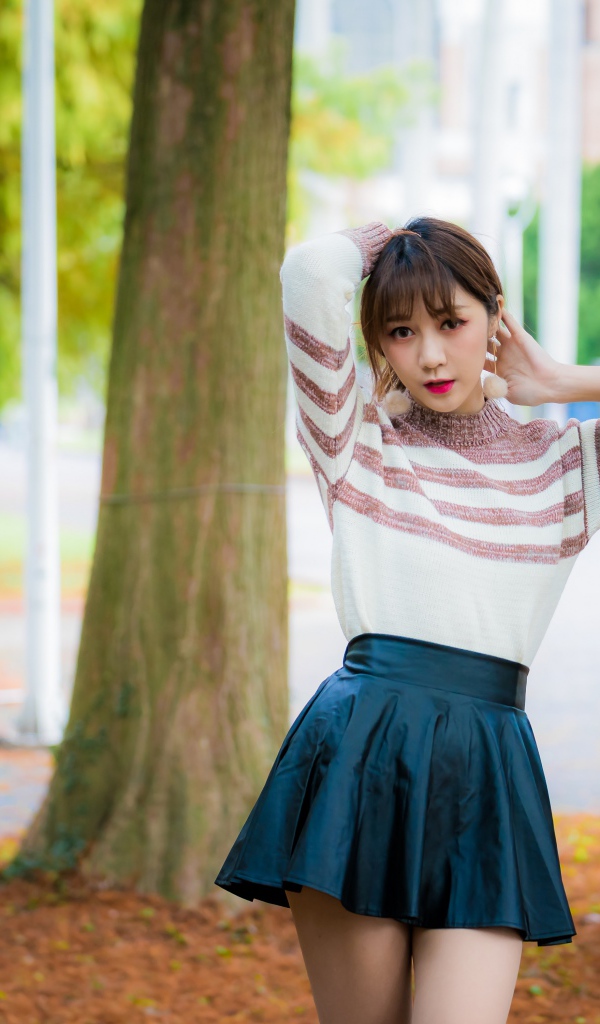 Девушка азиатка стоит в короткой юбке у дерева
