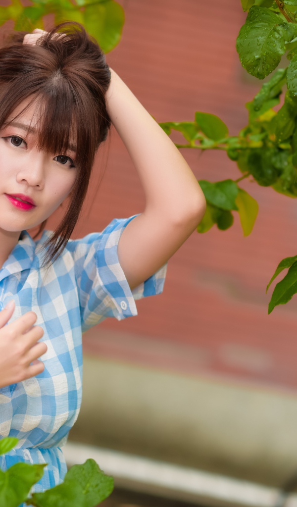 Азиатка в клетчатой рубашке стоит у зеленого дерева