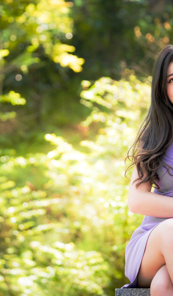 Молодая девушка азиатка сидит на лавке в парке