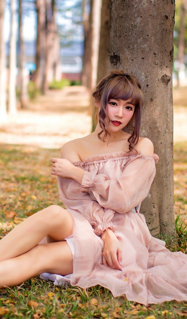 Красивая девушка азиатка в платье сидит под деревом