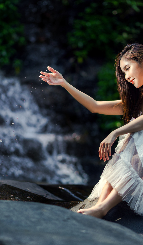 Красивая девушка азиатка в белом платье сидит у воды