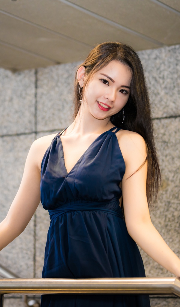 Красивая азиатка в черном платье стоит у перил