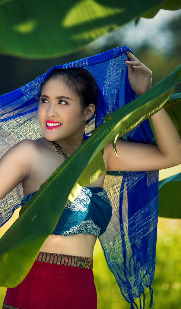 Красивая девушка азиатка с синим палантином у зеленых листьев