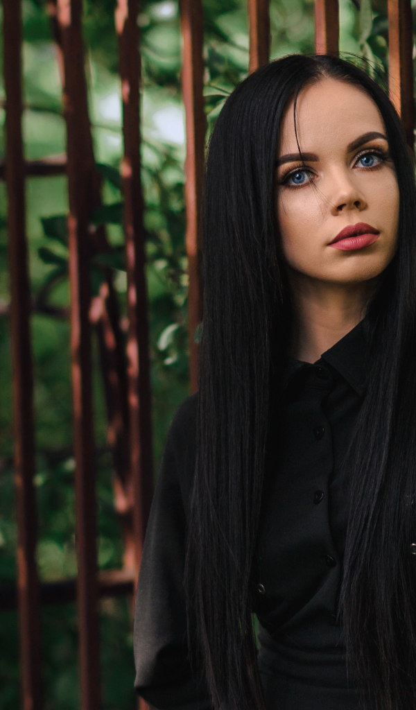 Красивая голубоглазая девушка в черном платье у железного забора