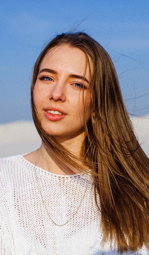 Красивая голубоглазая девушка в белом свитере на фоне голубого неба