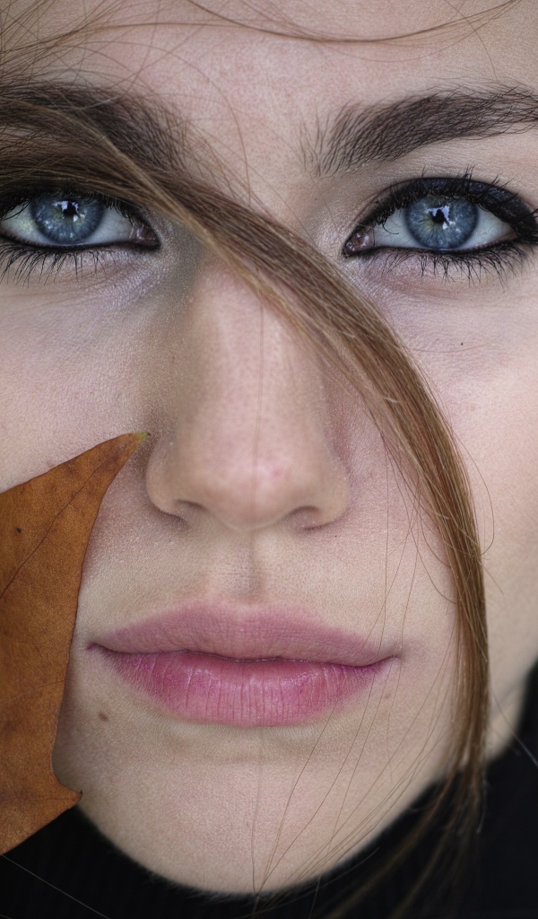 Красивая голубоглазая девушка с желтым листом у лица