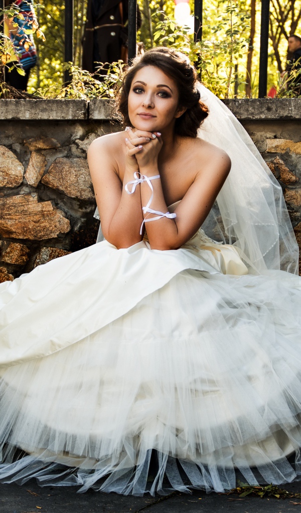 Красивая невеста в белом платье сидит на лавке