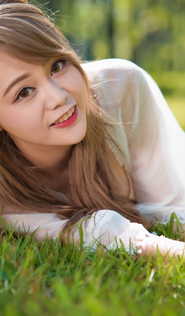 Красивая кареглазая девушка азиатка лежит на зеленой траве
