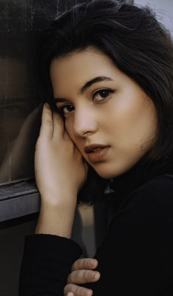 Красивая кареглазая девушка стоит у окна