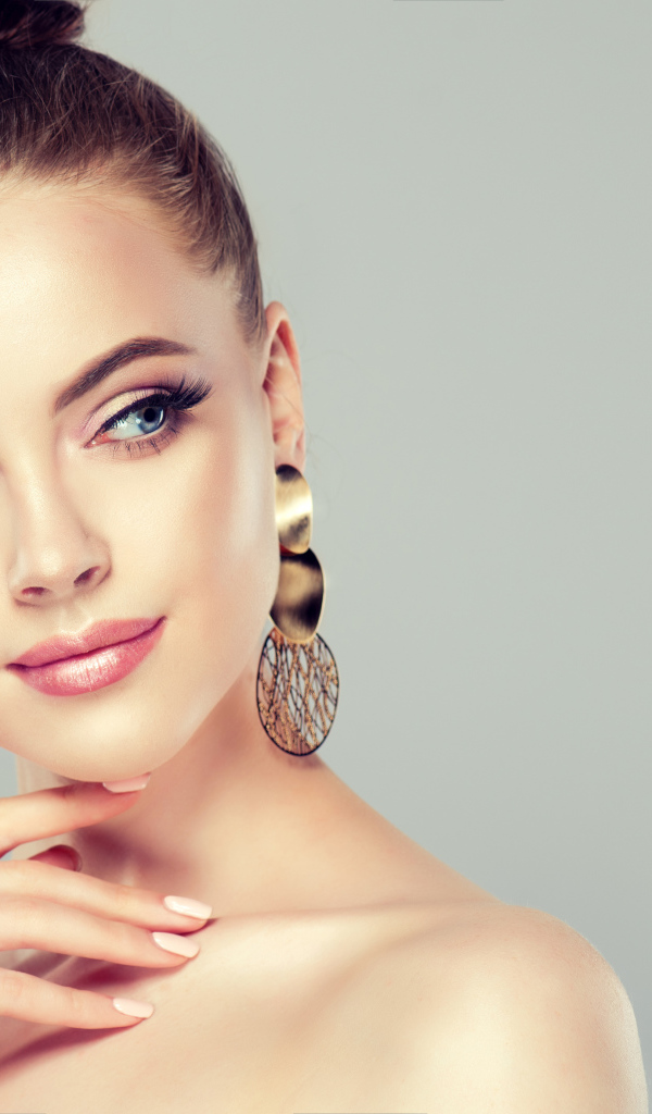 Красивая девушка шатенка с золотыми серьгами в ушах на сером фоне