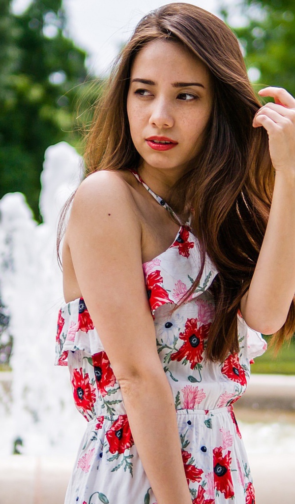 Красивая шатенка в цветастом платье у фонтана летом