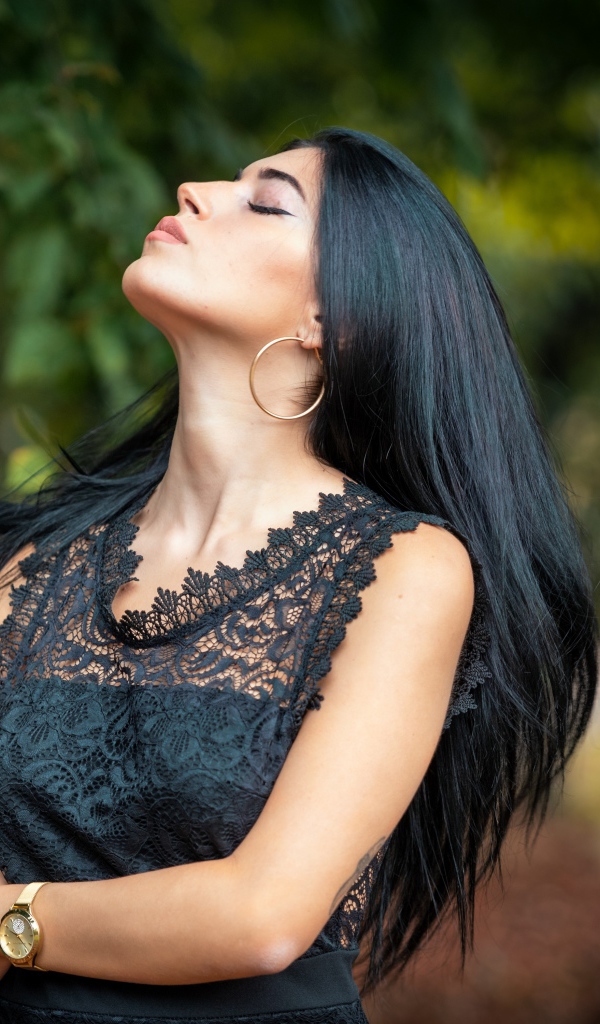Красивая брюнетка в черном платье с закрытыми глазами в парке