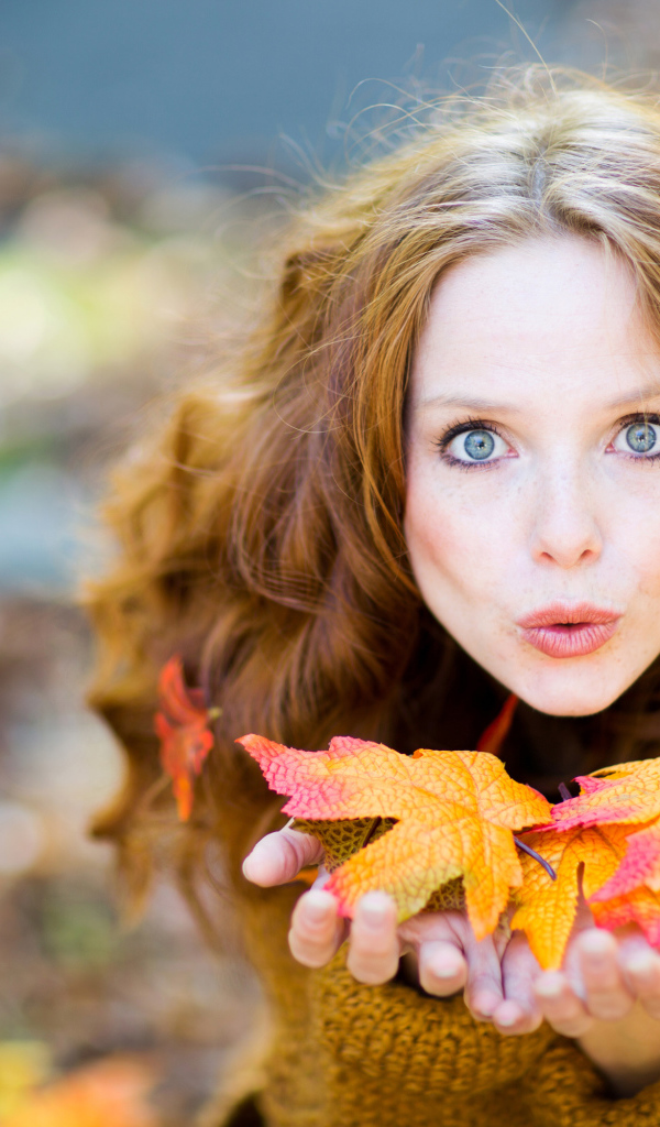 Красивая девушка сдувает листья с ладоней