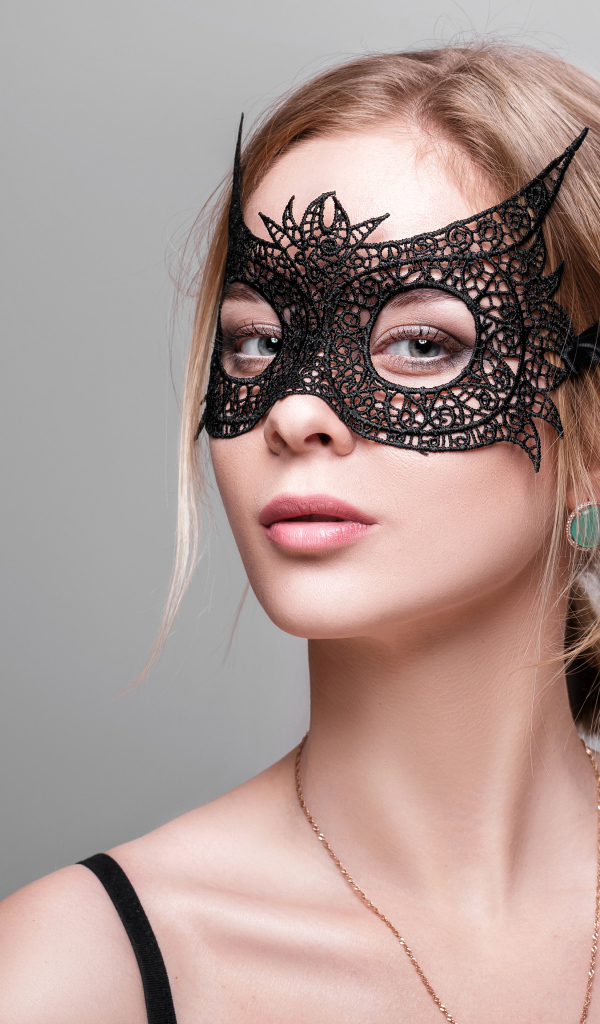 Красивая девушка в черной маске на сером фоне