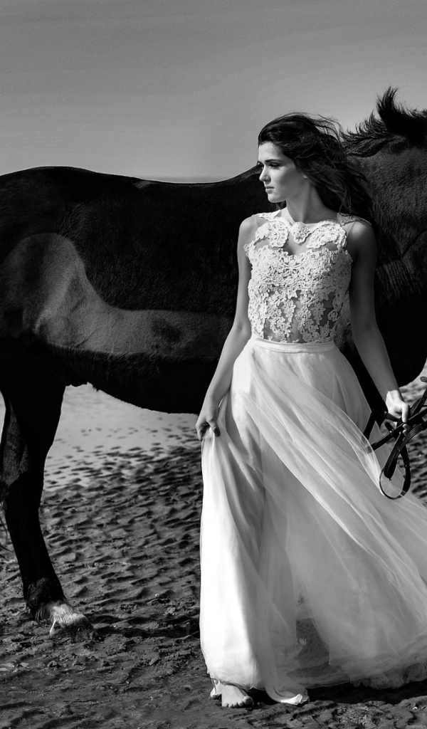 Красивая девушка в свадебном платье с лошадью на берегу моря