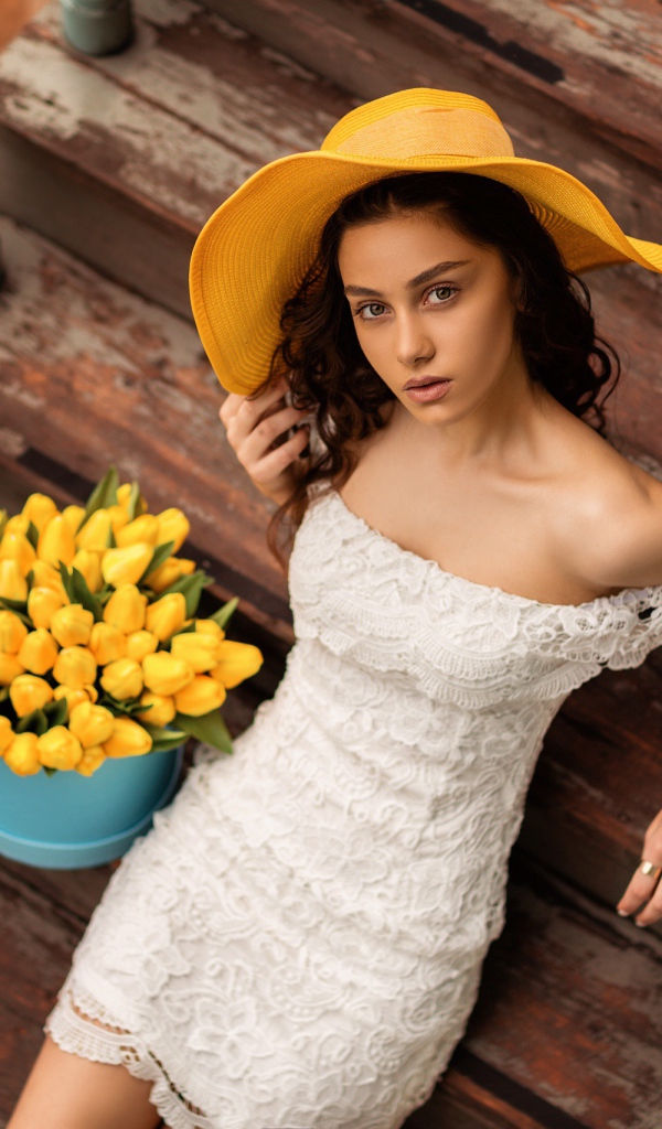 Красивая девушка в белом платье и желтой шляпе на ступеньках с букетом тюльпанов