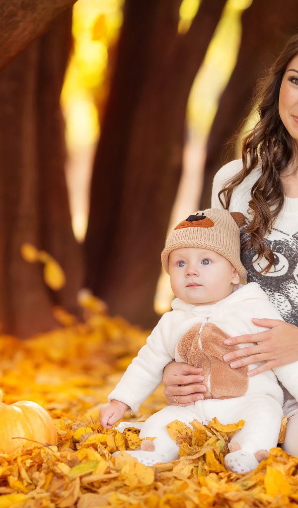 Красивая девушка сидит с грудным ребенком на опавшей листве