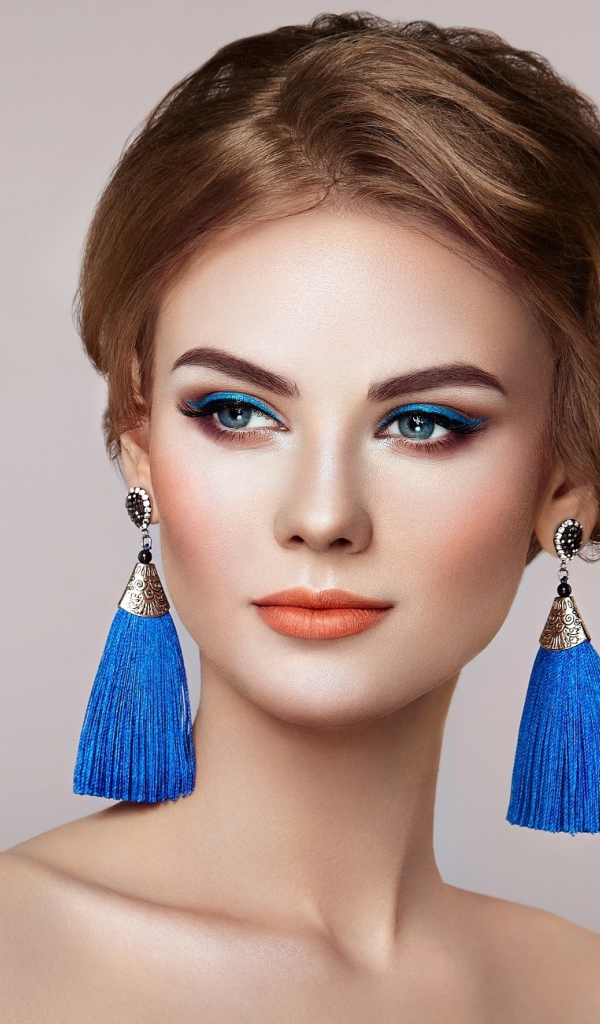 Красивая девушка с синими сережками на сером фоне