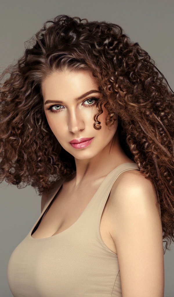 Красивая девушка с накрученными волосами на сером фоне