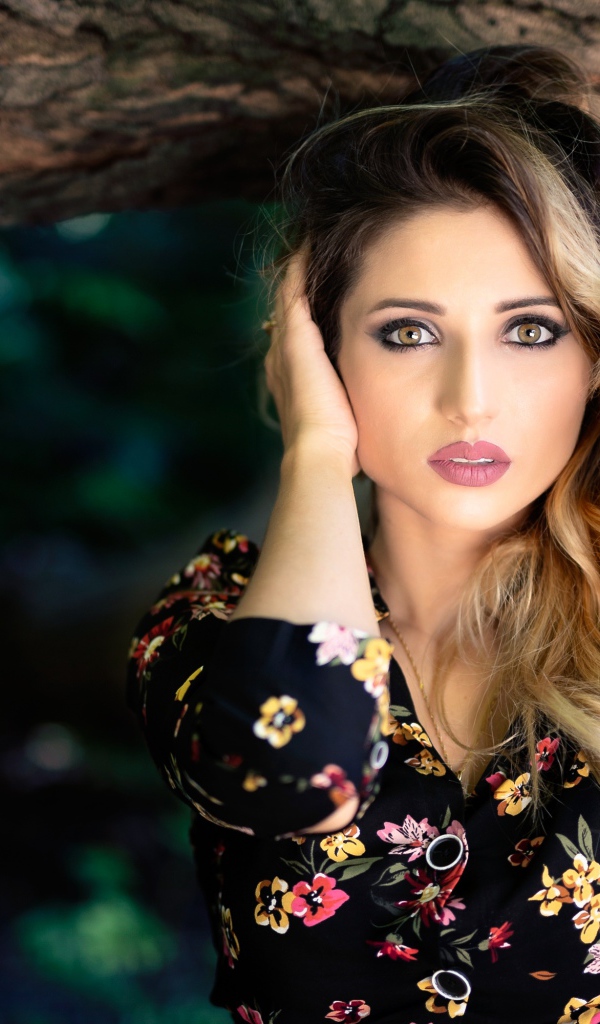 Красивая девушка с руками в волосах у дерева