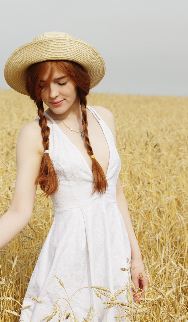 Красивая рыжеволосая девушка гуляет по полю с пшеницей