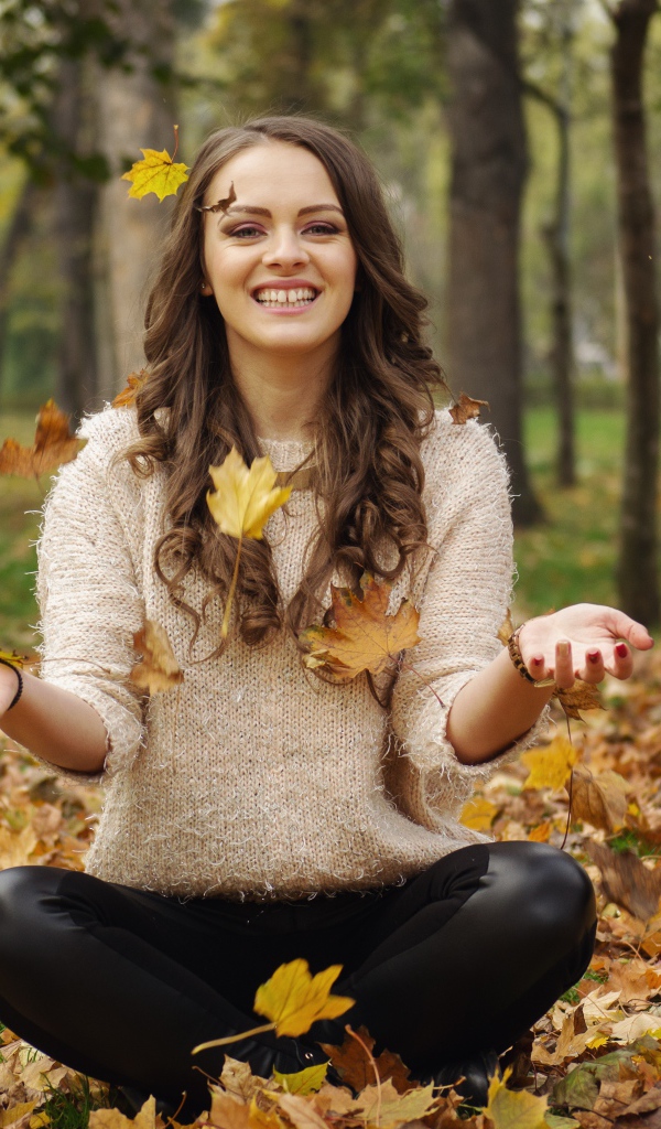Красивая улыбающаяся девушка сидит на земле с желтыми листьями