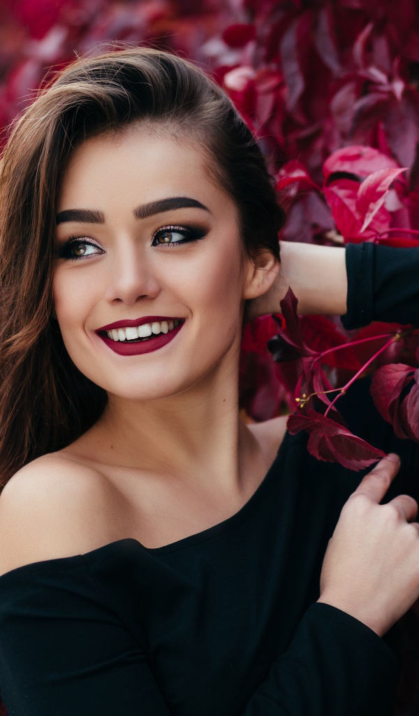 Красивая улыбающаяся длинноволосая девушка у стены с декоративным виноградом