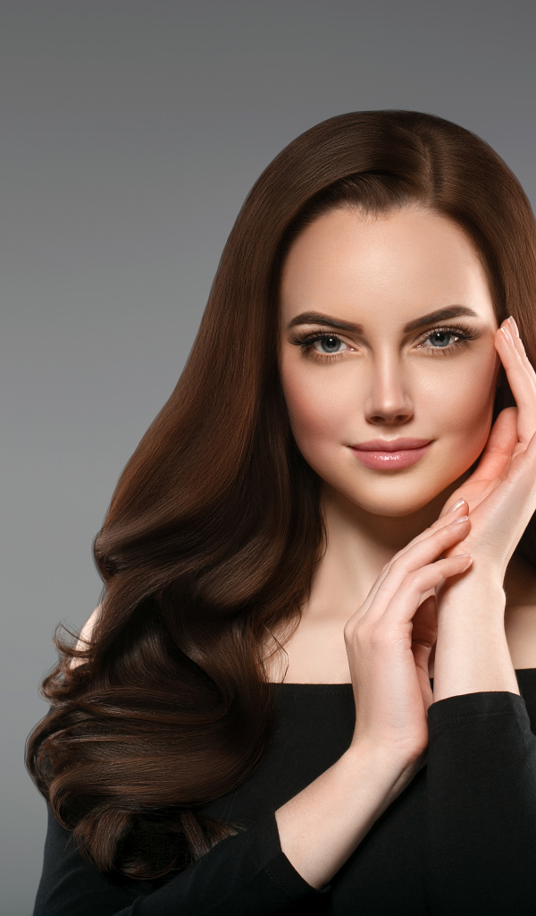 Красивая нежная длинноволосая шатенка  с руками у лица на сером фоне