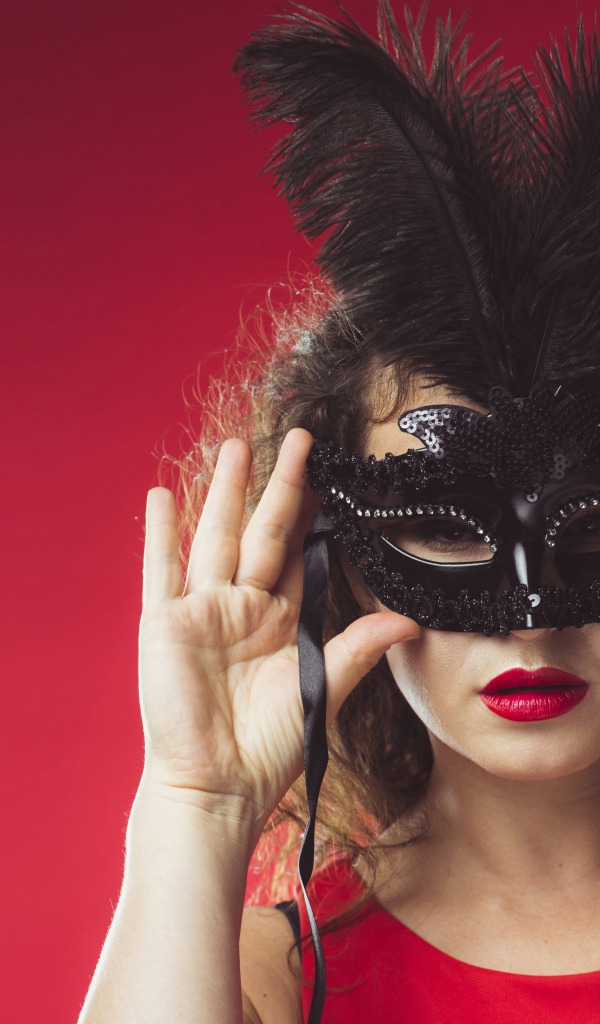 Красивая женщина в черной маске на красном фоне