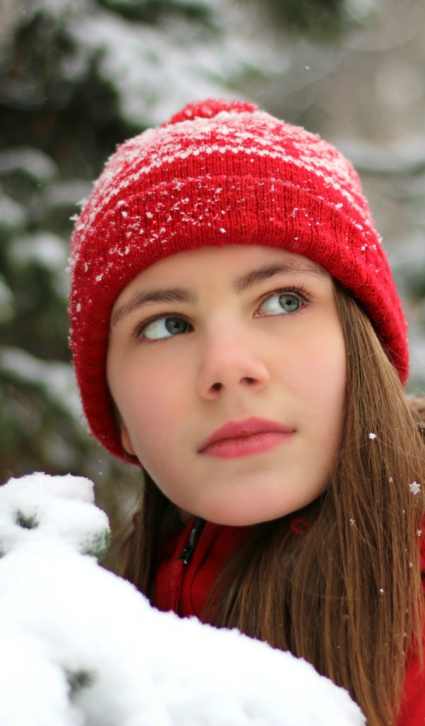 Красивая молодая девушка в красной шапке у заснеженной ели